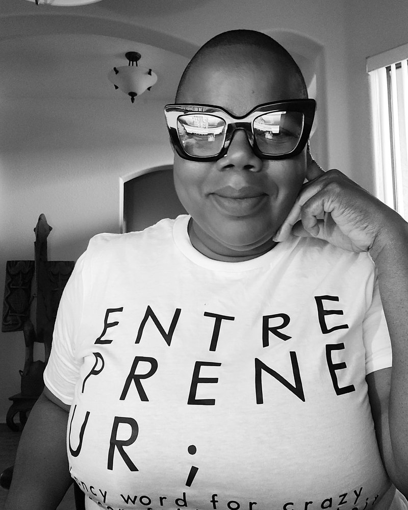 Black-and-white portrait of Luckie Daniels in large cat-eye glasses and a white ENTREPRENEUR t-shirt